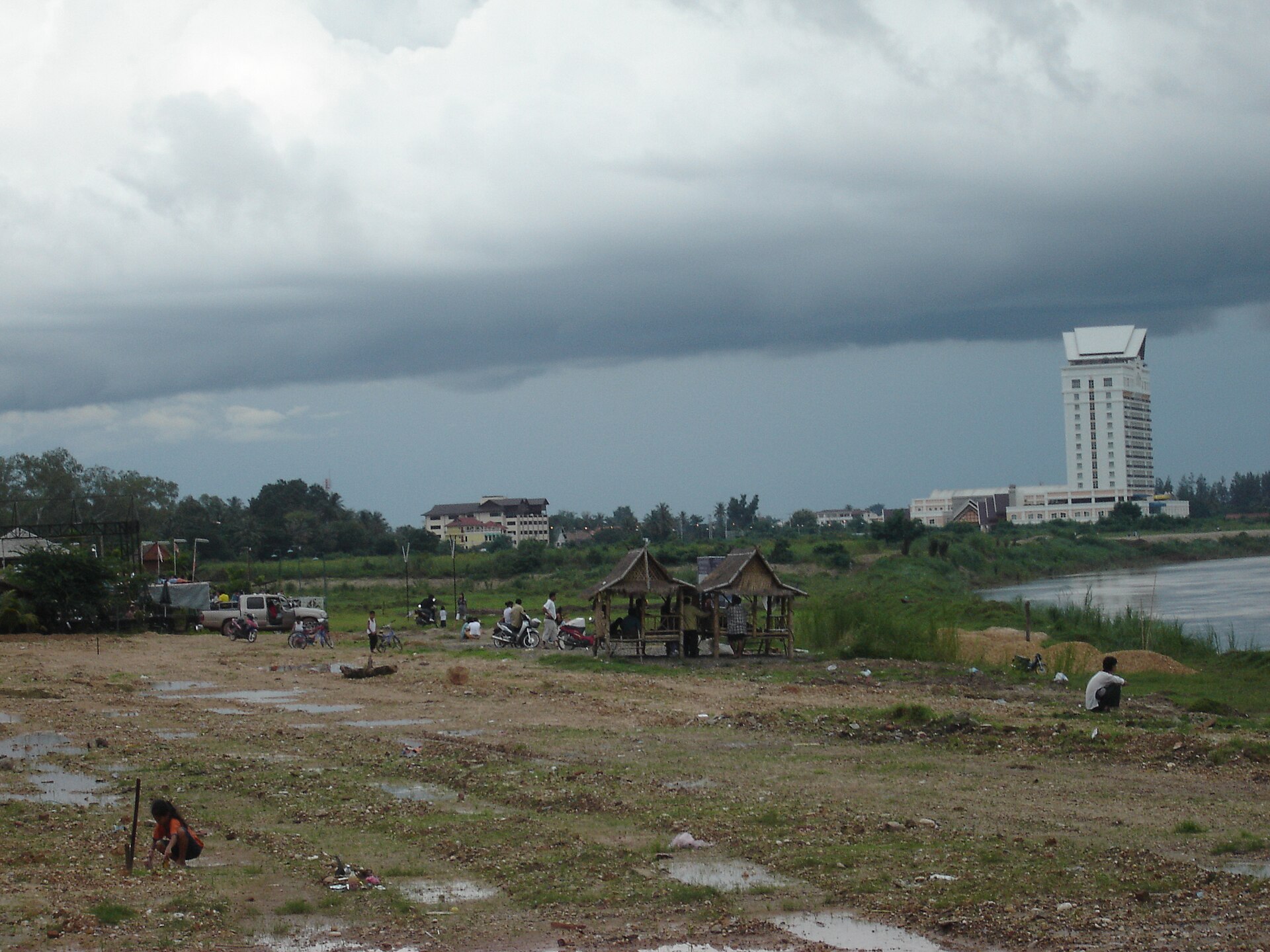 A street scene near the Mekong in Vientiane, with pickup trucks and motorbikes parked