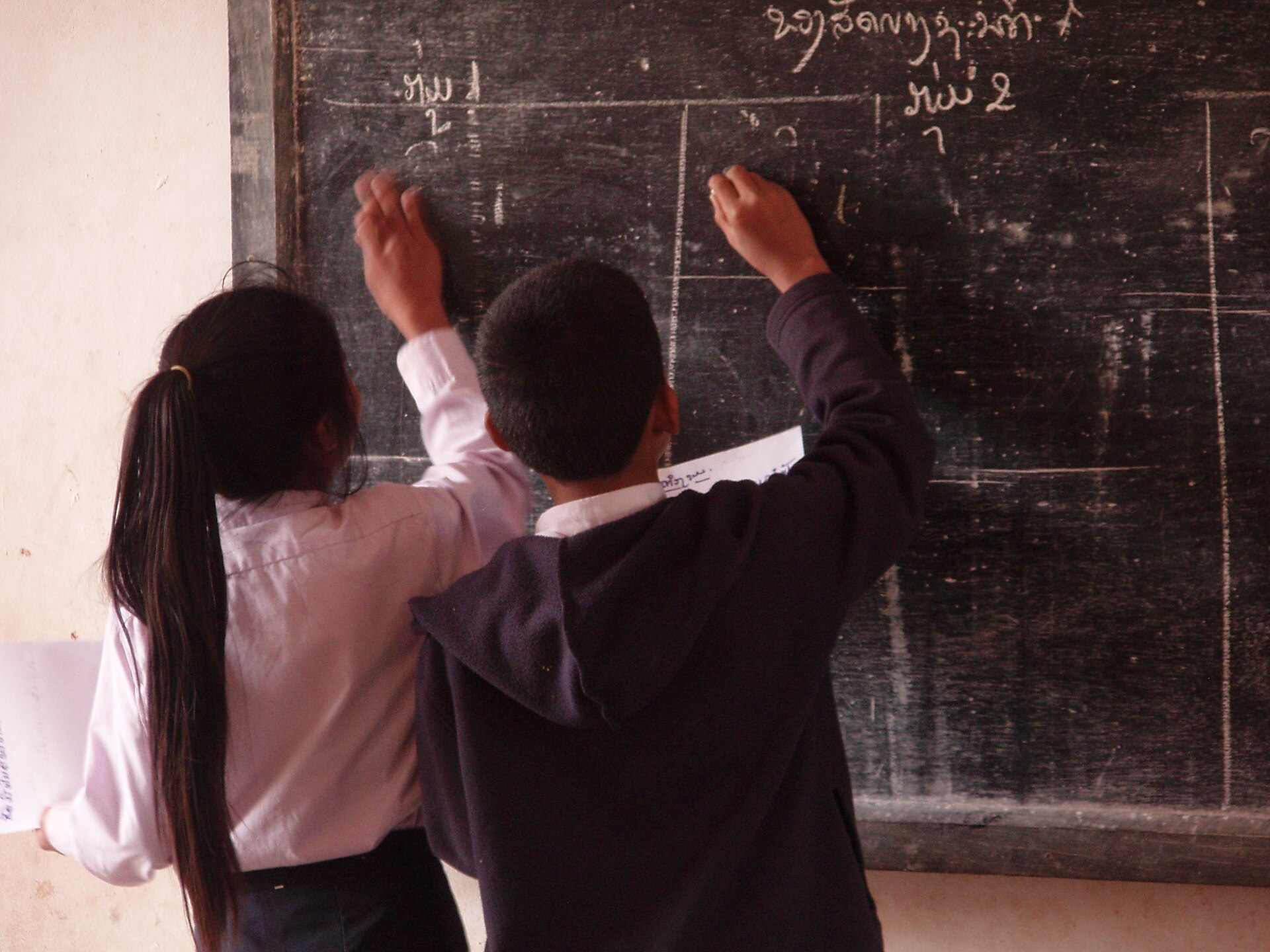 Two students writing on a blackboard in a Lao classroom