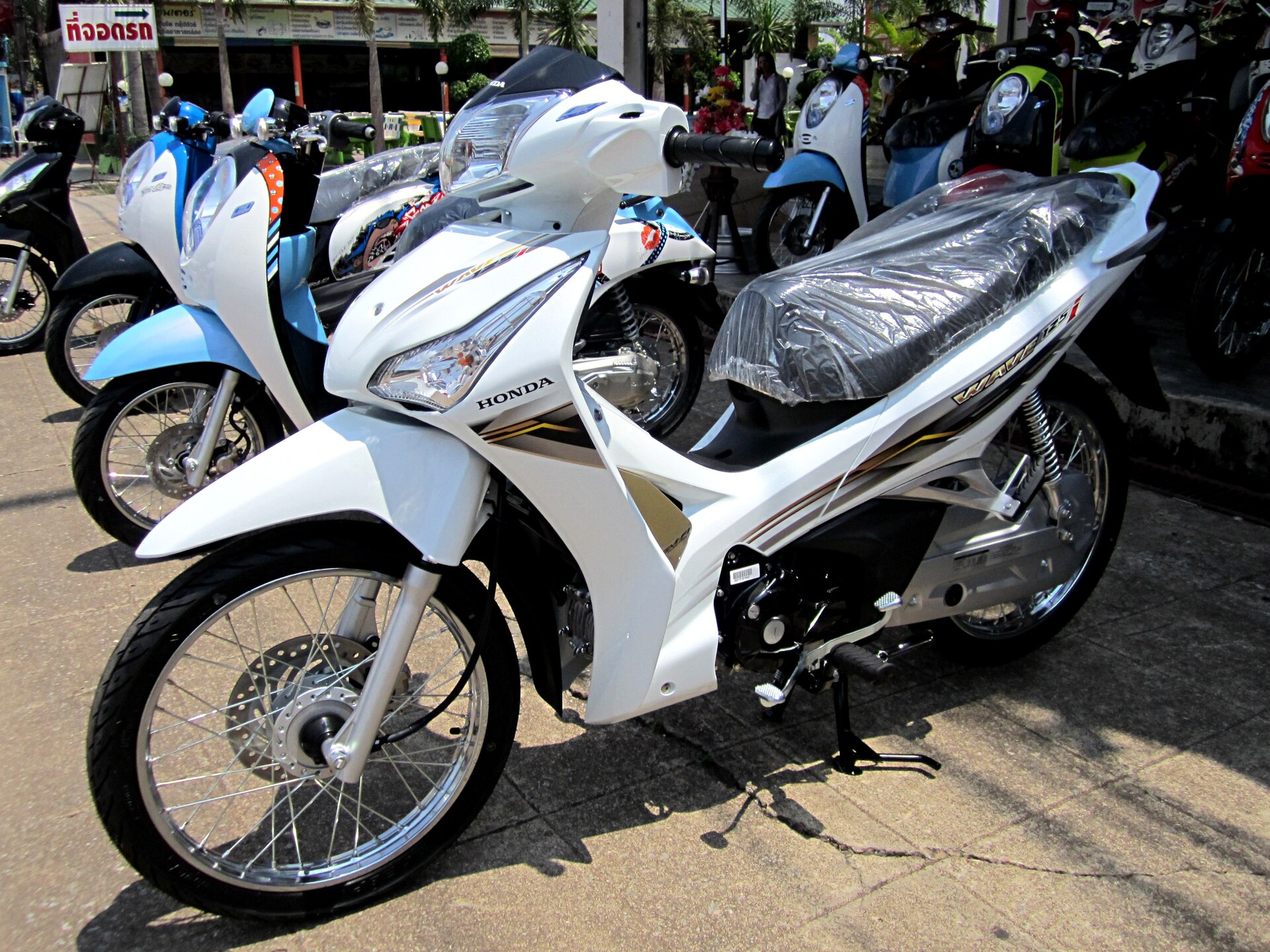 A white Honda Wave 125i on display among other scooters in a Thai showroom